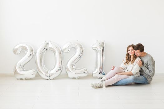 Holidays, festive and party concept - Happy loving couple holds silver 2021 balloons on white background. New Year celebration.