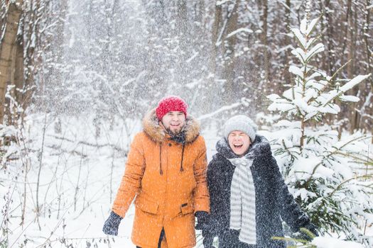 Love, season, friendship and people concept - happy young man and woman having fun and playing with snow in winter forest