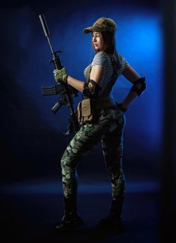 a woman in a military airsoft uniform in a vest with an American automatic rifle on a dark background