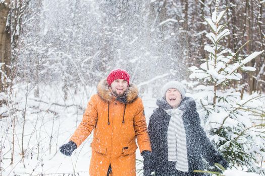 Love, season, friendship and people concept - happy young man and woman having fun and playing with snow in winter forest