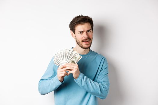 Handsome young man showing money and looking pleased. Guy dancing with dollars, earn income, standing over white background