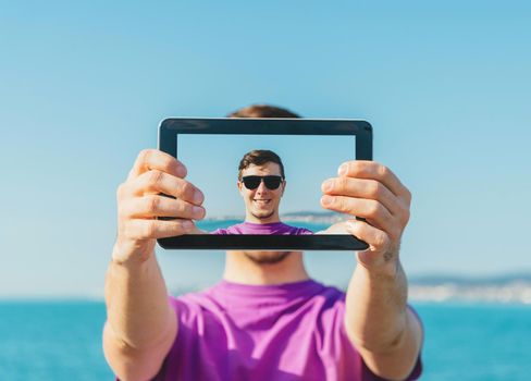 Man doing a self-portrait with him digital tablet on beach