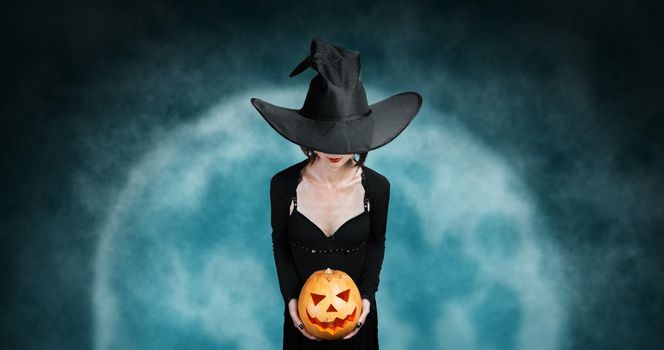 Witch holds Halloween pumpkin at midnight