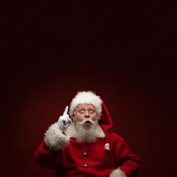 Full length portrait of Santa Claus pointing up to background with copy space for text