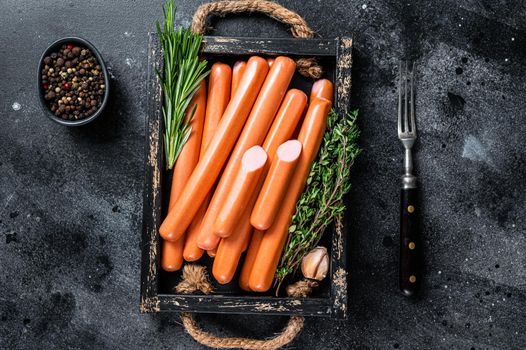 Frankfurter sausages in a wooden tray with herbs. Black background. Top view