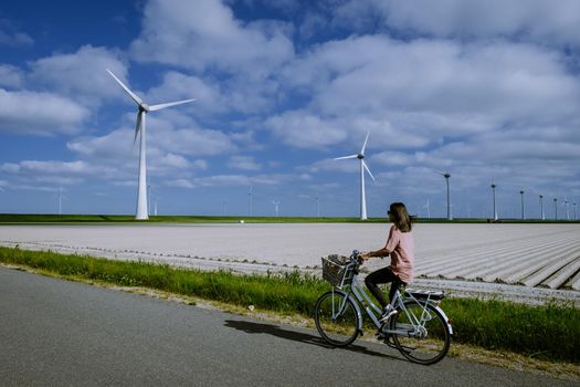 young woman electric green bike bicycle by windmill farm , windmills isolated on a beautiful bright day Netherlands Flevoland Noordoostpolder