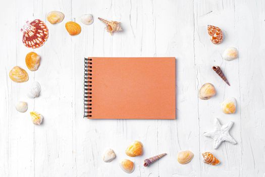Open notepad with sea shells on white wooden background