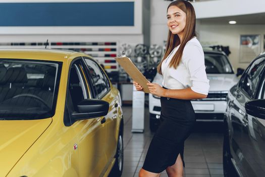 Attractive young female car dealer standing in showroom