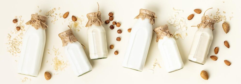 Non dairy plant based milk in bottles and ingredients on light background. Alternative lactose free milk substitute, flat lay