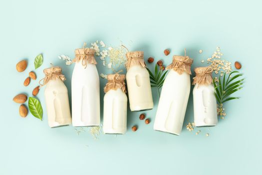 Non dairy plant based milk in bottles and ingredients on turquoise background. Alternative lactose free milk substitute, flat lay