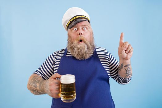Emotional sailor with overweight holds beer and gestures on light blue background