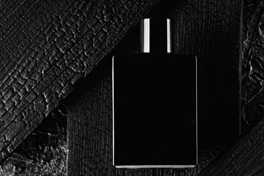 This is a promotional photo of eau de toilette or perfume in a dark style.Black bottle on the background of a burnt tree