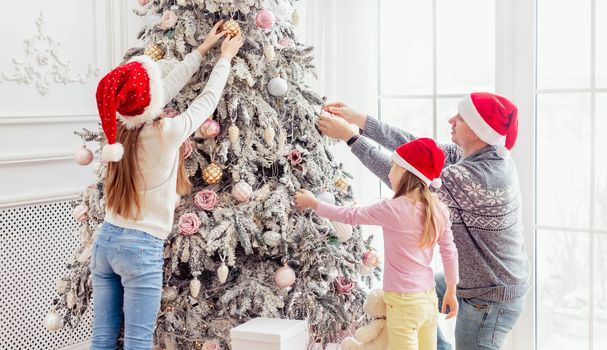 Father and daughters decorating christmas tree