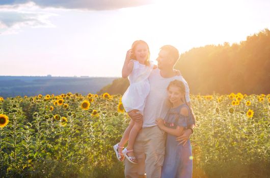 daddy with little daughters in sunflower field