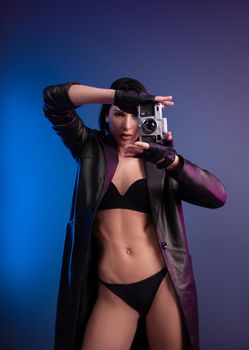 a brunette photographer girl in underwear and a leather raincoat poses in a photo studio with a camera