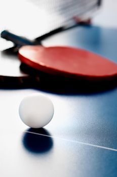 Two tennis rackets and a white ball lie on a tennis table near the net. Active recreation and playing ping pong.