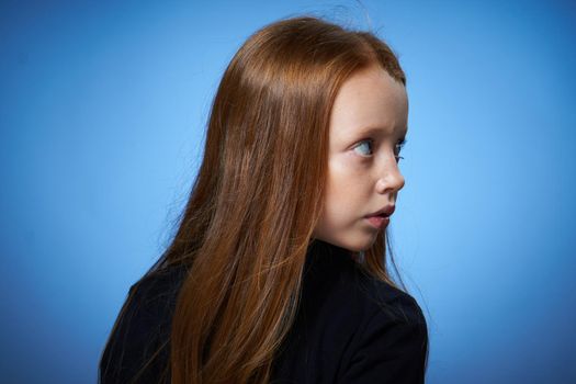 redhead girl with freckles on her face posing close-up blue background