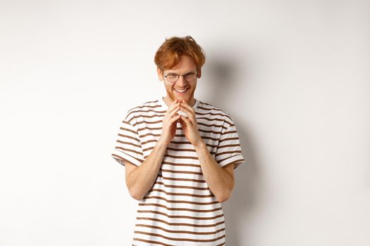 Portrait of redhead man looking like evil genius, steeple fingers and chuckling devious, scheming some plan, standing over white background