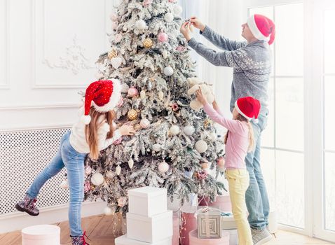 Father and daughters decorating christmas tree