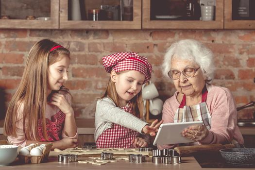 Grandma with granddaughters looking for a recipe in tablet