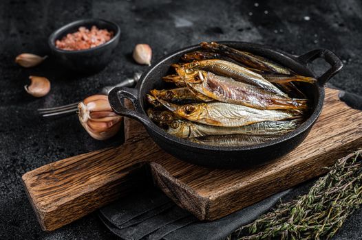 Hot Smoked sprat and Anchovy fishes in pan. Black background. Top view