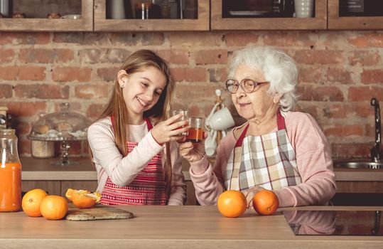 Granny with granddaughter tasting orange juice at kitchen