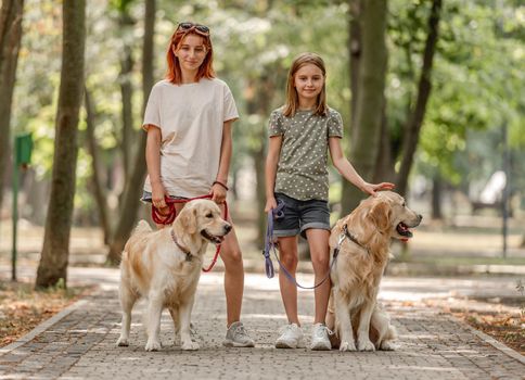 Girls with golden retriever dogs in the park. Sisters walking with pets doggies at nature