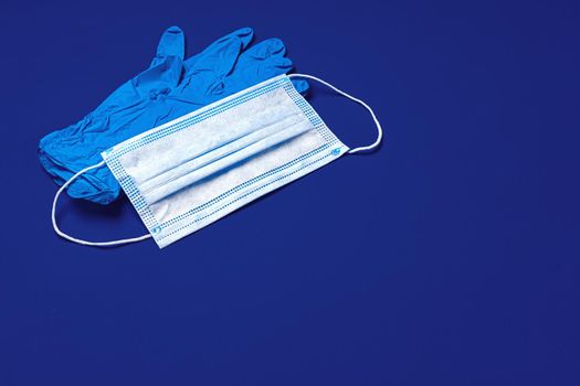 Medical gloves and surgical protective face mask on dark blue background