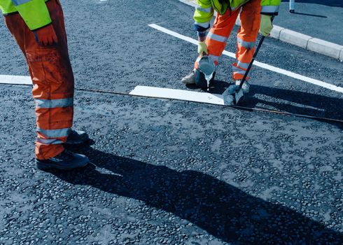 Roadworker applying thermoplastic road marking on the freshly laid tarmac during new roundabout and road construction