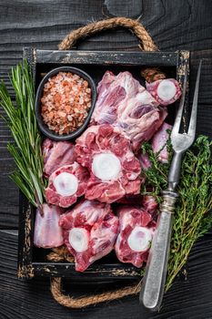 Raw veal beef Oxtail Meat in wooden tray with thyme. Black wooden background. Top view