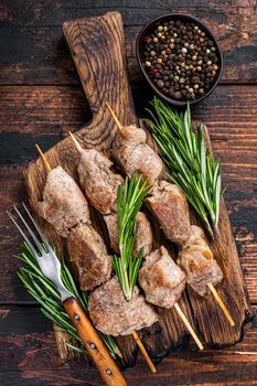 Pork meat Shish kebab on skewers with herbs on a wooden board. Dark wooden background. Top view
