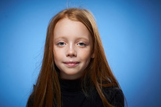 redhead girl with freckles on her face posing close-up blue background