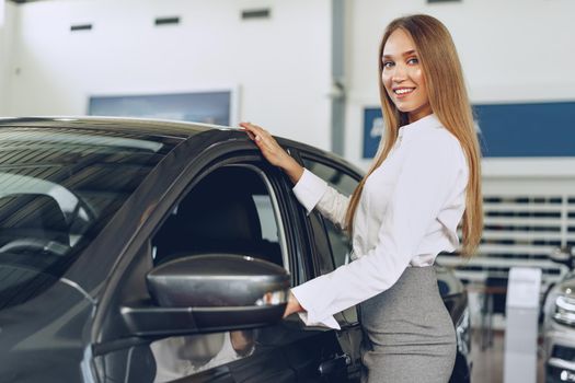 Beautiful young woman touching her new car with pleasure