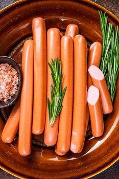 Frankfurter raw sausages in a rustic plate with herbs. Dark background. Top view