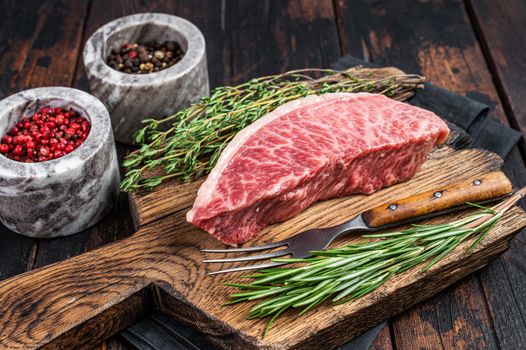 Wagyu A5 raw rump or sirloin steak, kobe beef meat on a butchery board. Dark wooden background. Top view
