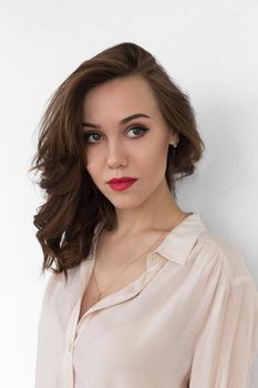 Beautiful caucasian girl with red lips and dreamy gaze in beige blouse looks thoughtfully aside, on white background.