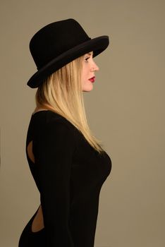 Fashion photo of beautiful lady in elegant black dress and hat stands sideways