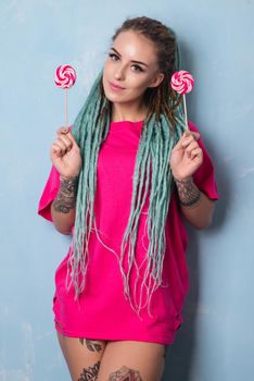 Cute girl in pink t-shirt with dreadlocks and tattoo holding lollipops