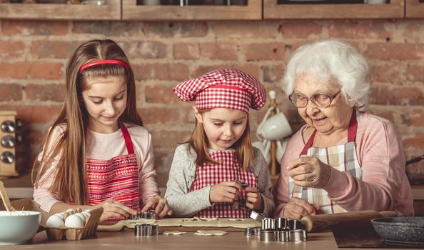 Little granddaughters help granny to bake cookies