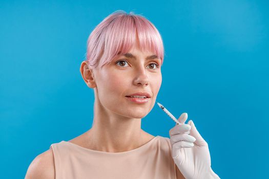 Beautiful woman with pink hair looking away while receiving botox injection in lips from beautician