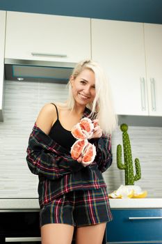 A woman in the kitchen in home clothes with a peeled pomelo fruit smiles
