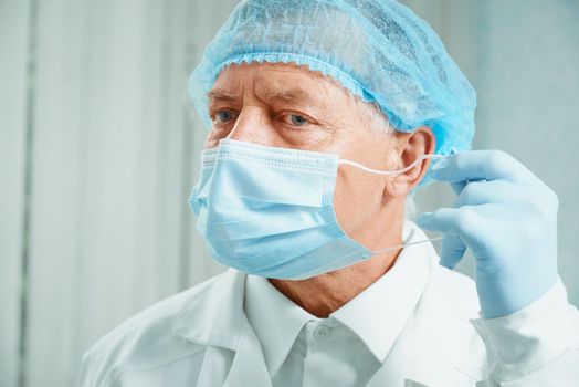 Older surgeon takes off his mask