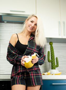 Woman in the kitchen in home clothes cleaning fruit pomelo with emotions