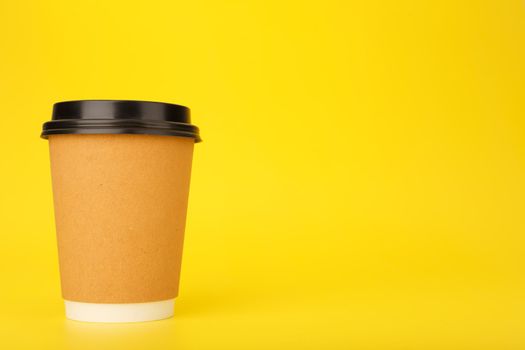 Minimal composition with brown cardboard cup of coffee on yellow background with copy space