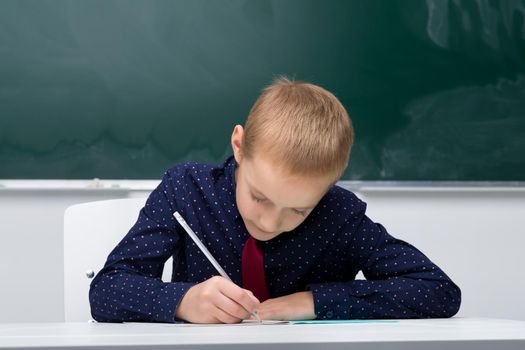 Schoolboy writes in a notebook sitting at a desk