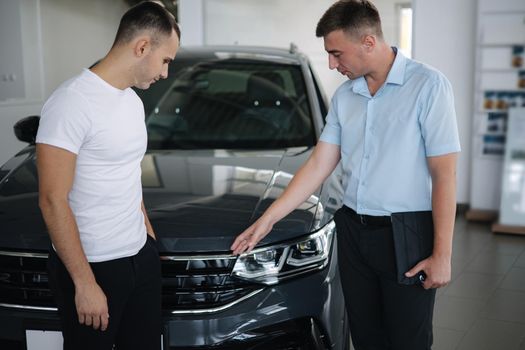 Salesperson selling cars at car dealership. Man choosing car in car showroom