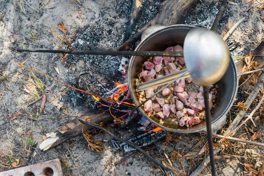 meat stewing in kettle on campfire