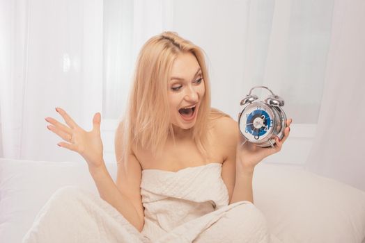 Shocked adult woman in bed with an alarm clock in hand