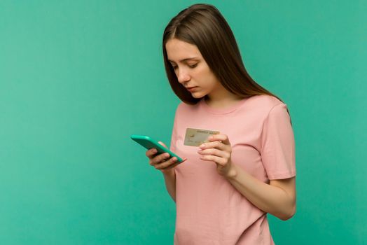 Photo of pleased happy screaming young woman posing isolated over blue wall background using mobile phone holding credit card.