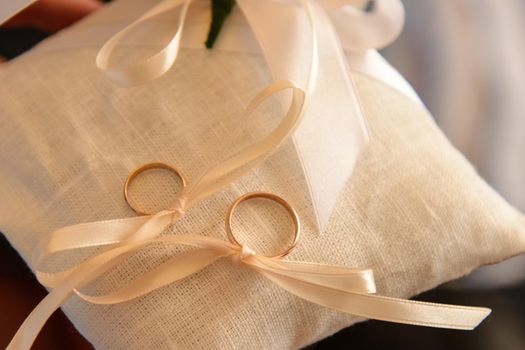 two wedding rings on a cushion tied with ribbon